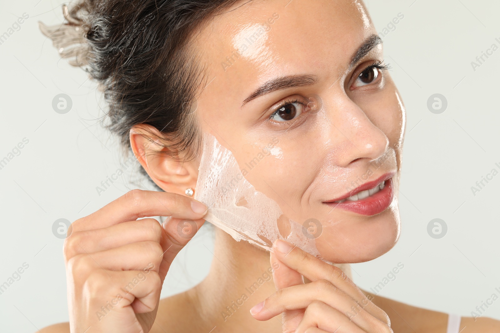 Photo of Beautiful woman peeling off face mask on light grey background, closeup