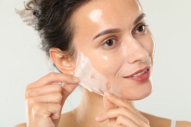 Beautiful woman peeling off face mask on light grey background, closeup