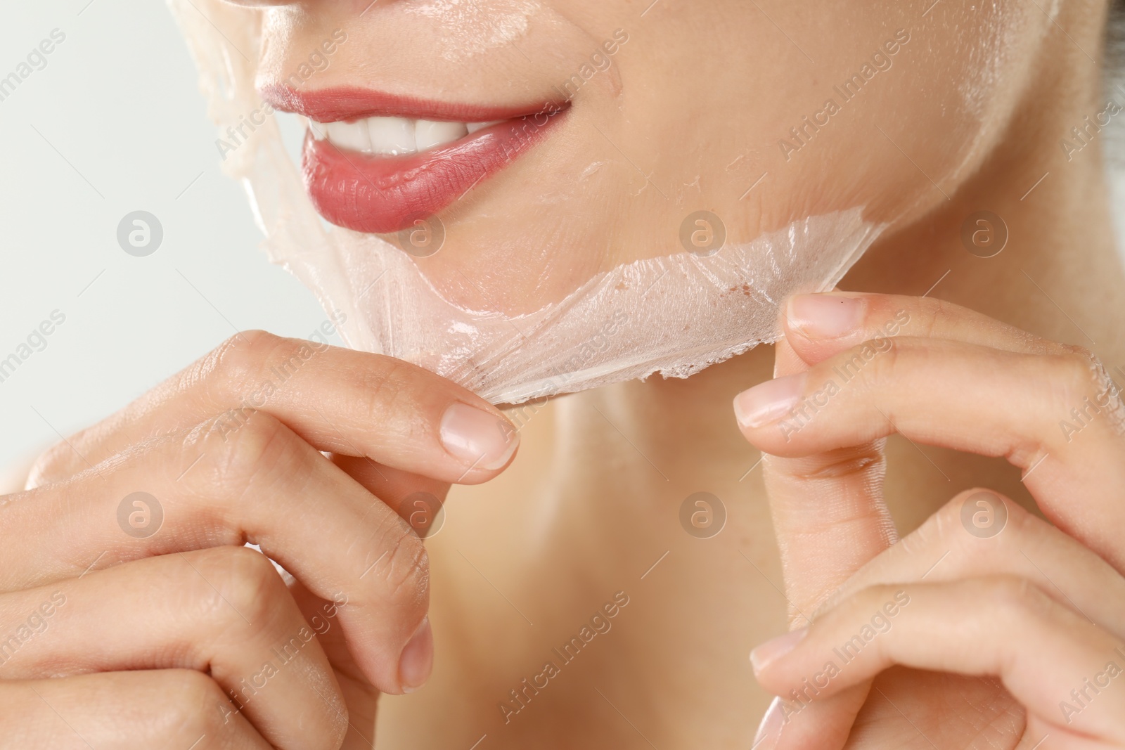 Photo of Smiling woman peeling off face mask on light grey background, closeup