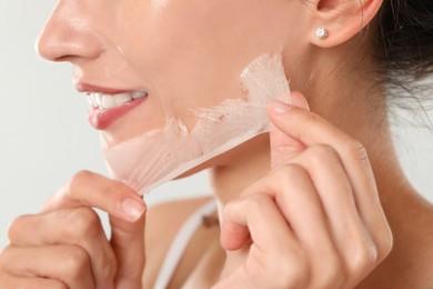 Smiling woman peeling off face mask on light grey background, closeup