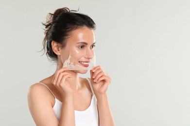 Smiling woman peeling off face mask on light grey background. Space for text