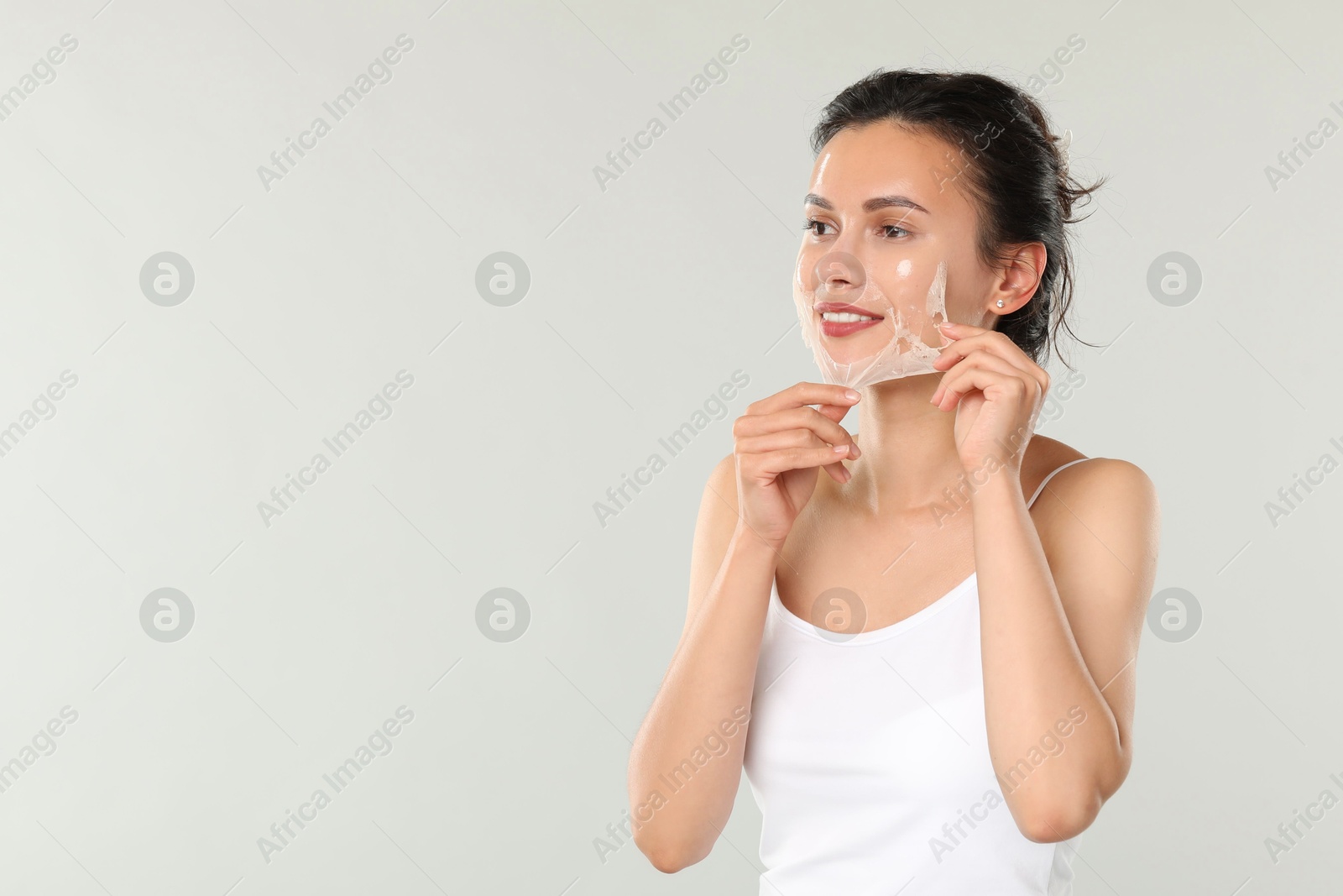 Photo of Smiling woman peeling off face mask on light grey background. Space for text