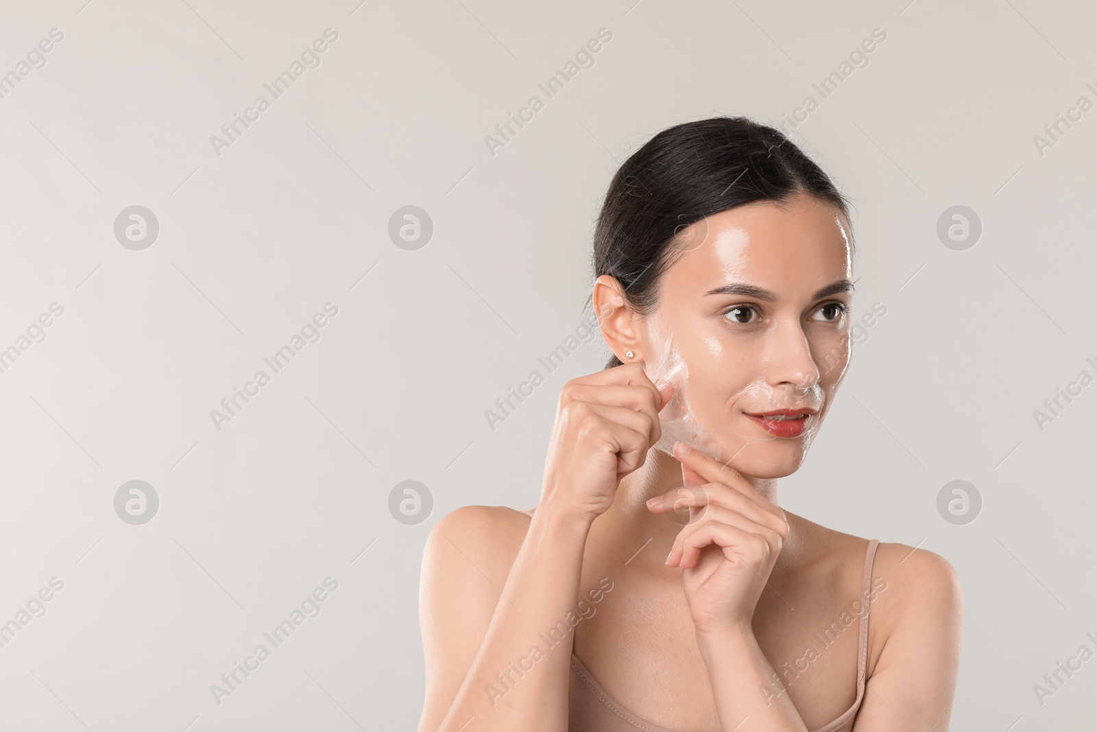 Photo of Smiling woman peeling off face mask on light grey background. Space for text