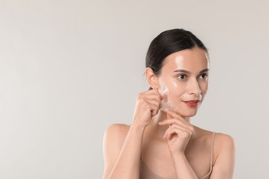 Smiling woman peeling off face mask on light grey background. Space for text