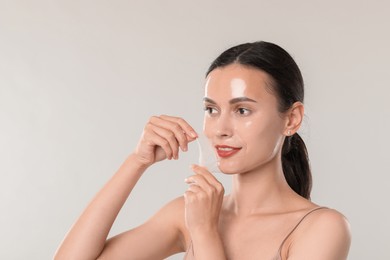 Photo of Smiling woman peeling off face mask on light grey background