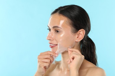 Smiling woman peeling off face mask on light blue background. Space for text