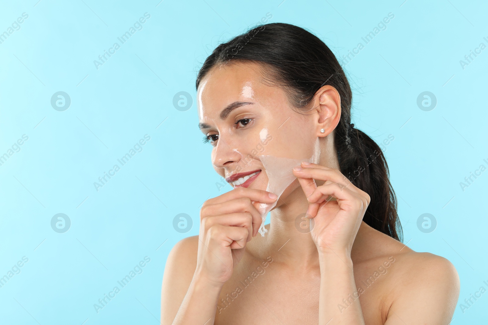 Photo of Smiling woman peeling off face mask on light blue background. Space for text