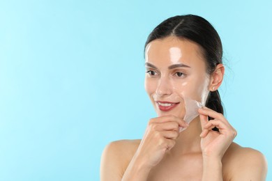 Smiling woman peeling off face mask on light blue background. Space for text