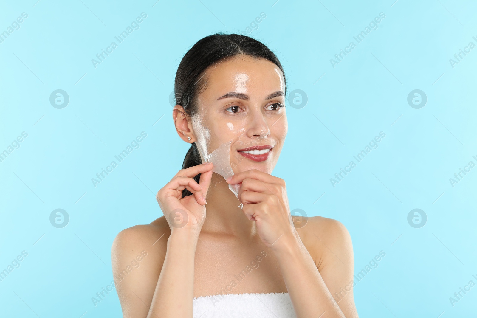 Photo of Smiling woman peeling off face mask on light blue background