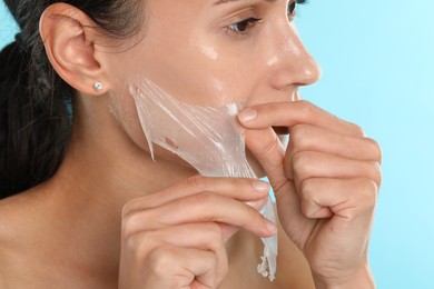 Beautiful woman peeling off face mask on light blue background, closeup