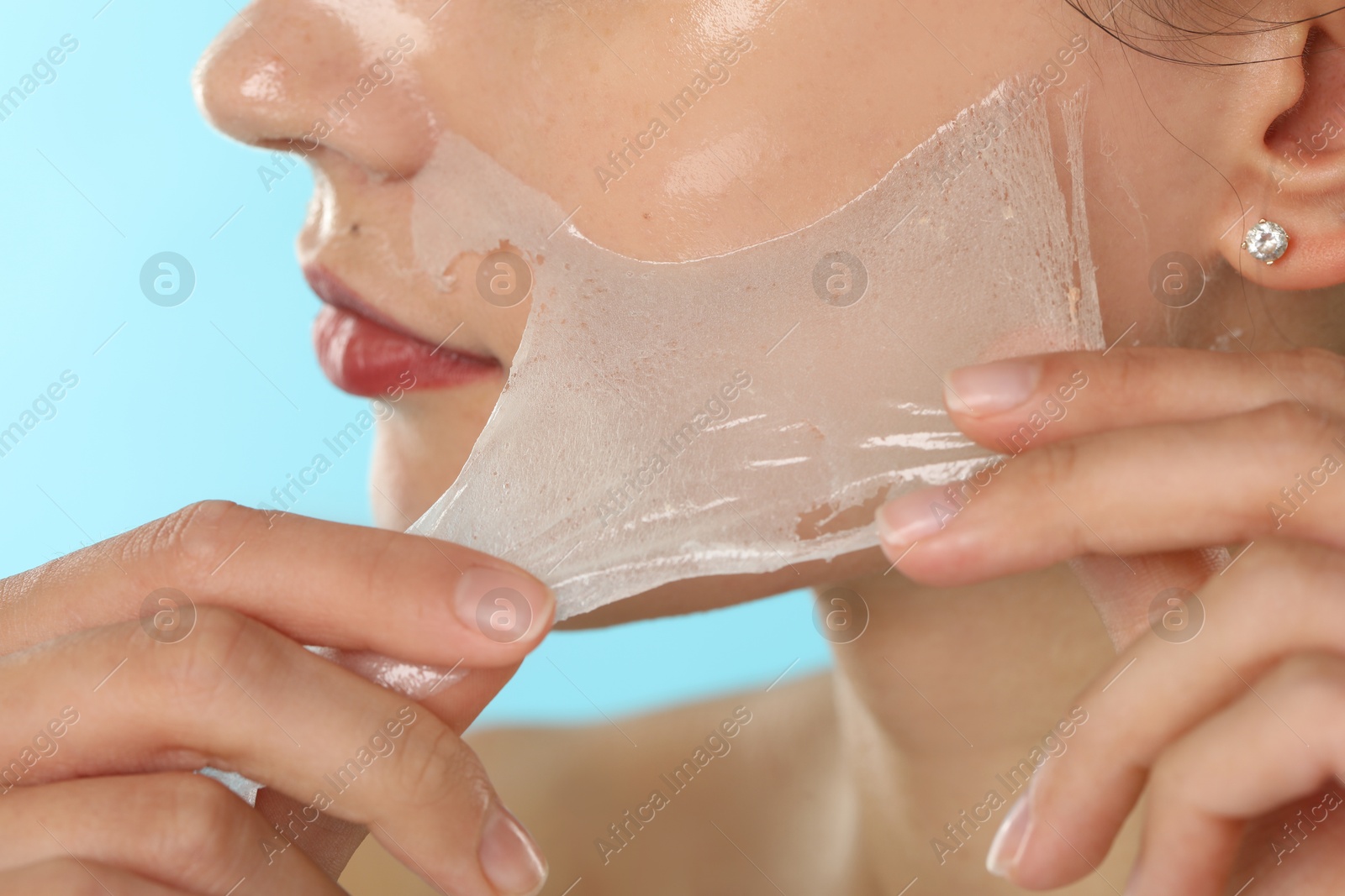 Photo of Woman peeling off face mask on light blue background, closeup