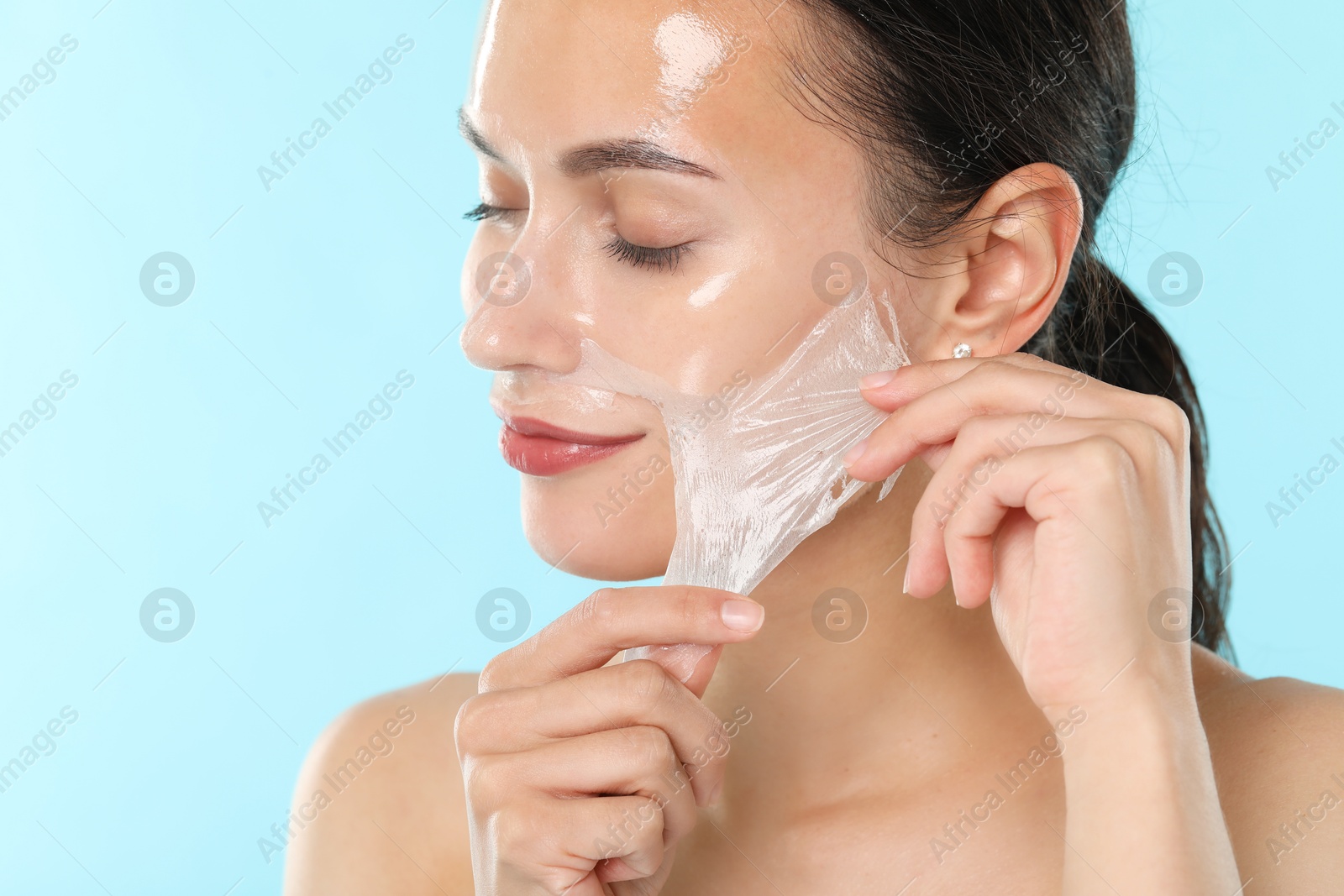 Photo of Beautiful woman peeling off face mask on light blue background, closeup