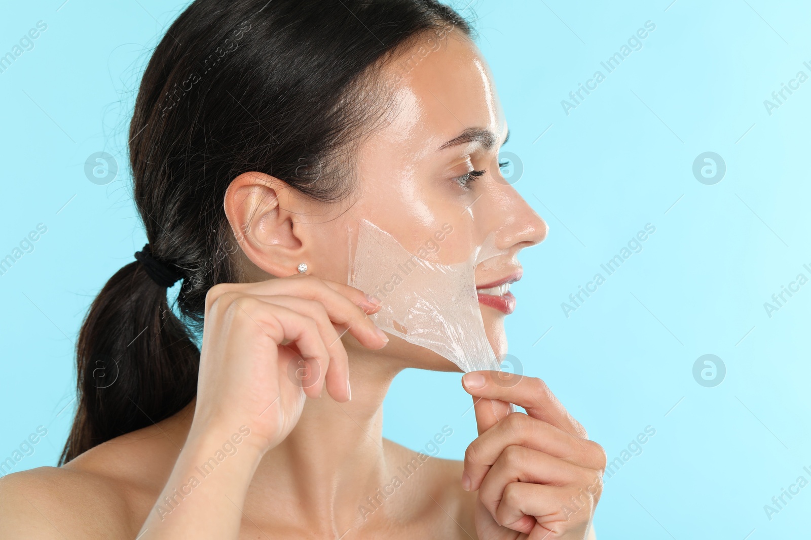 Photo of Beautiful woman peeling off face mask on light blue background, closeup