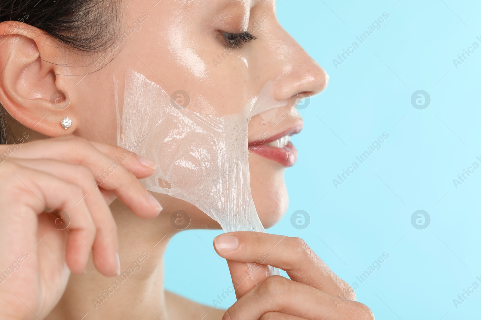 Photo of Beautiful woman peeling off face mask on light blue background, closeup