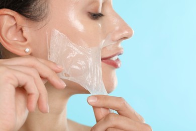 Beautiful woman peeling off face mask on light blue background, closeup