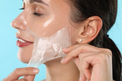 Smiling woman peeling off face mask on light blue background, closeup