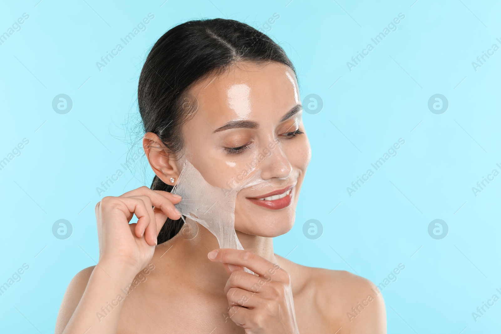 Photo of Smiling woman peeling off face mask on light blue background