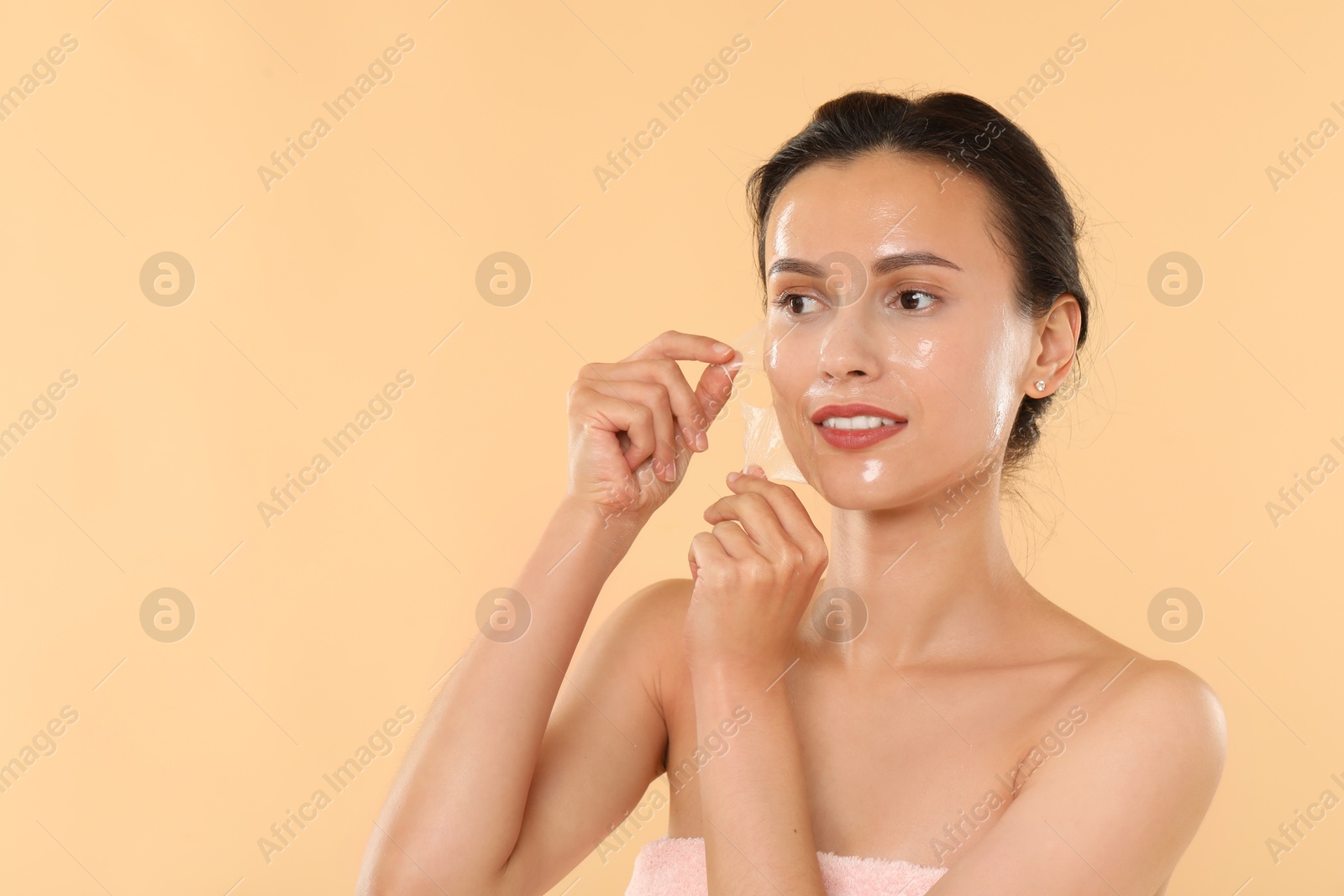 Photo of Beautiful woman peeling off face mask on beige background. Space for text