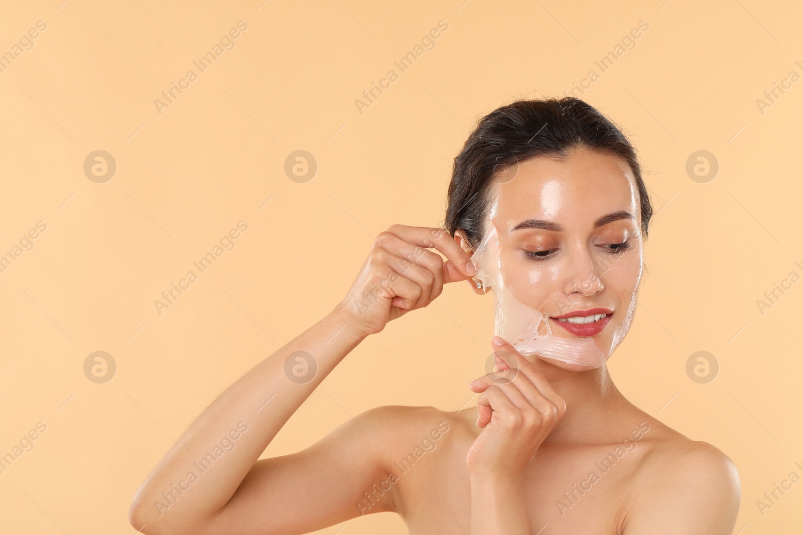 Photo of Smiling woman peeling off face mask on beige background. Space for text