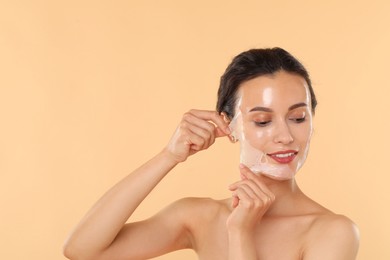 Smiling woman peeling off face mask on beige background. Space for text