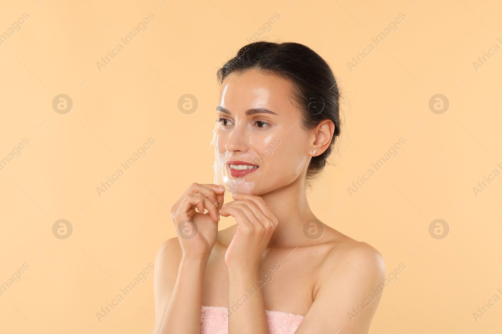 Photo of Beautiful woman peeling off face mask on beige background