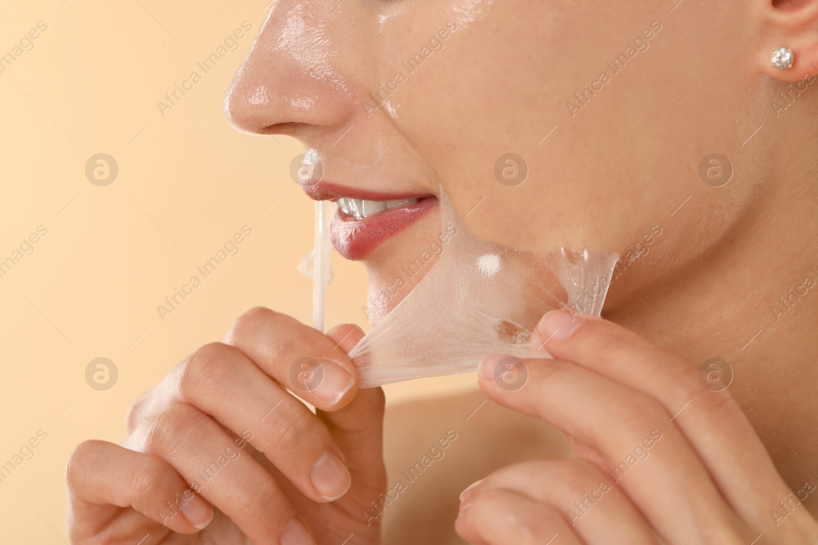 Photo of Woman peeling off face mask on beige background, closeup