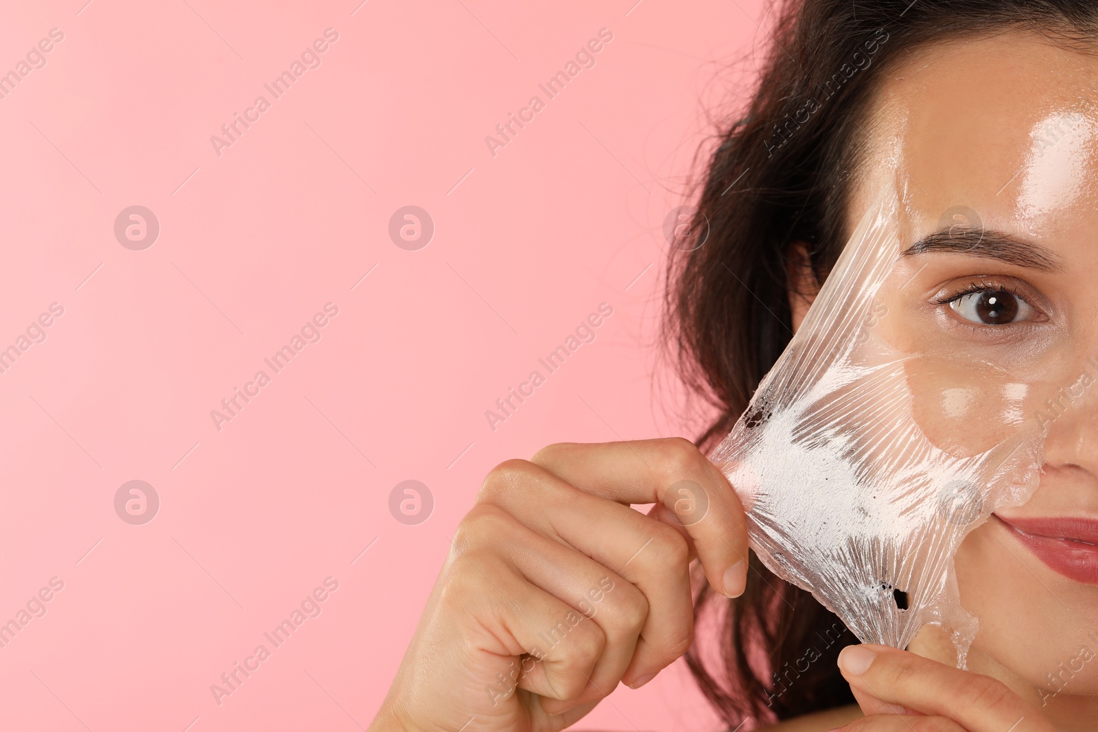 Photo of Woman peeling off face mask on pink background, closeup. Space for text