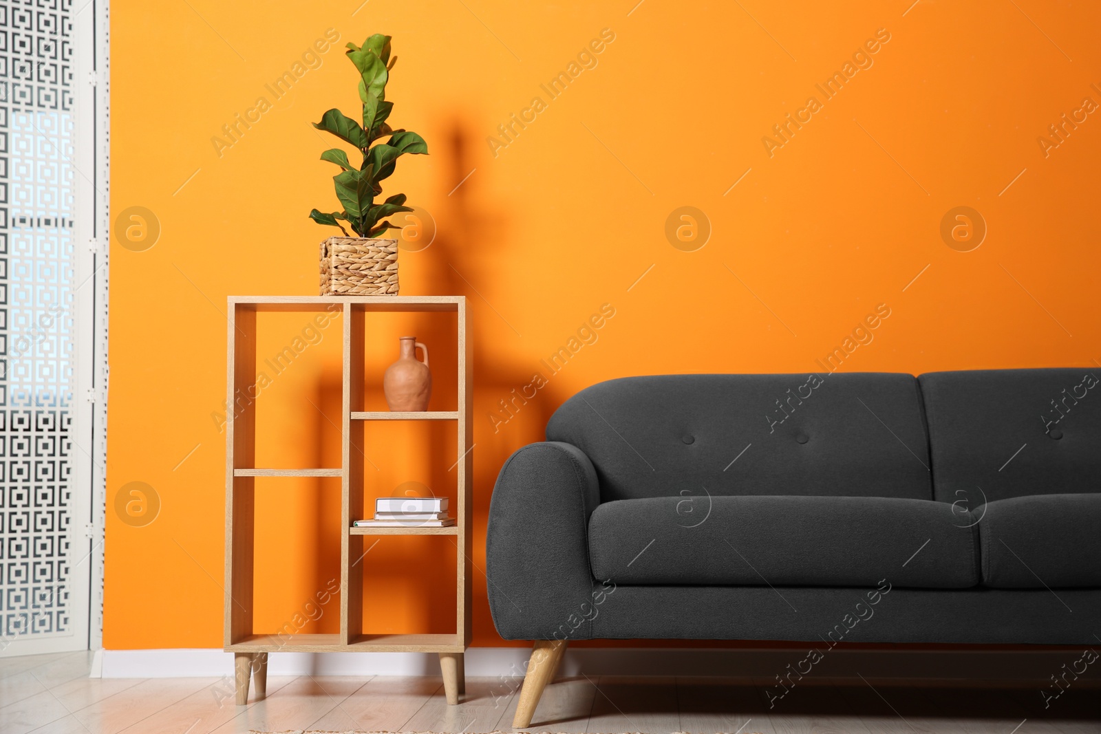 Photo of Stylish sofa and decor elements near orange wall in room