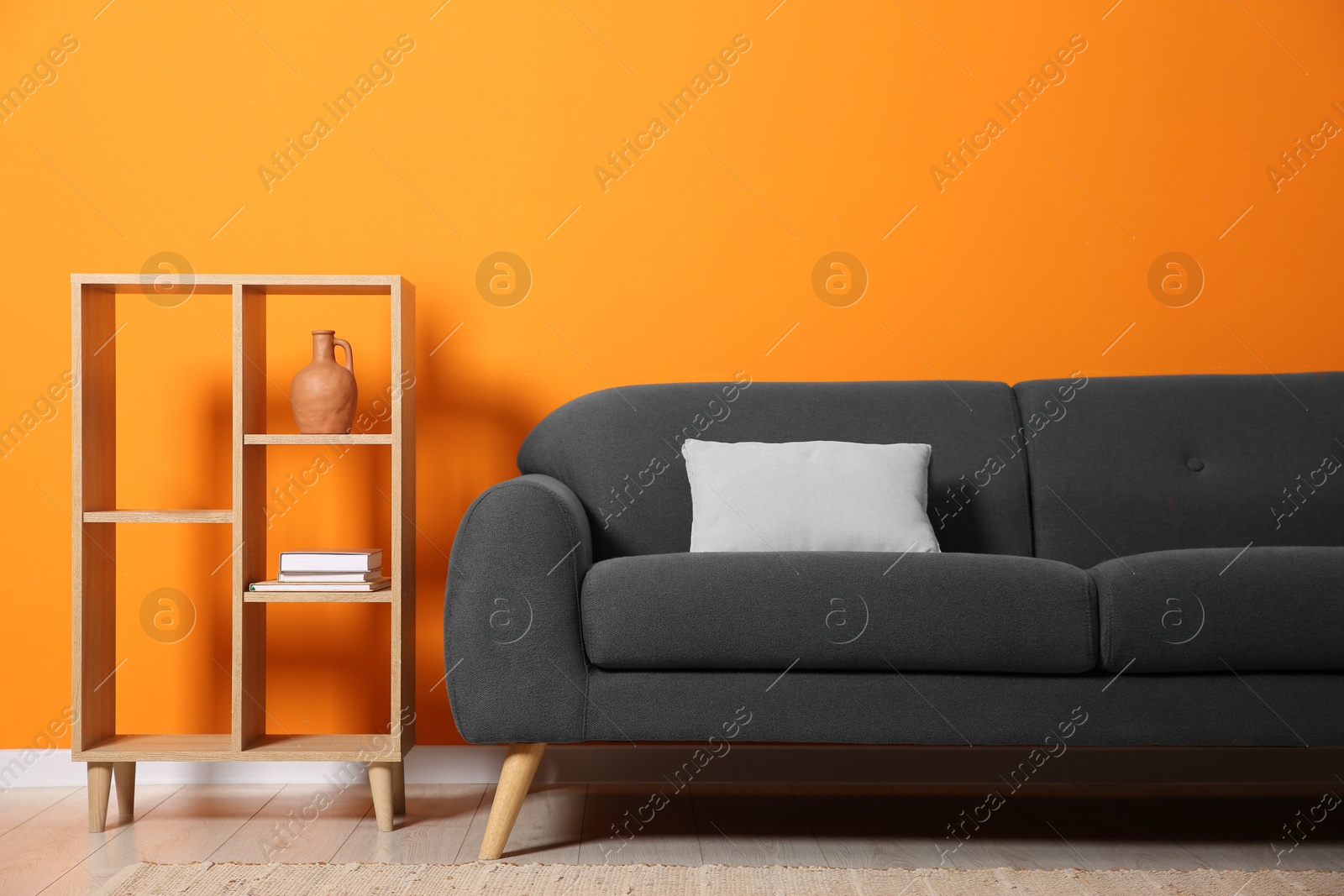 Photo of Stylish sofa with cushion and decor elements near orange wall in room