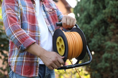 Photo of Man with extension cord reel outdoors, closeup