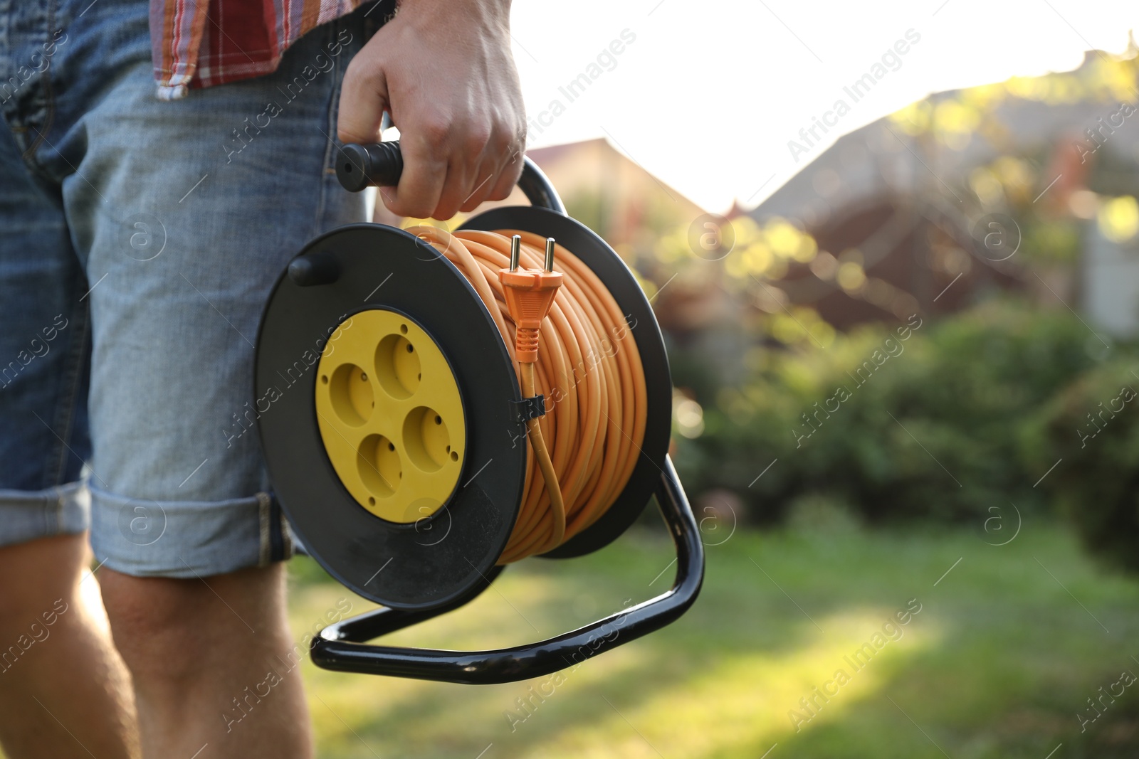 Photo of Man with extension cord reel outdoors on sunny day, closeup. Space for text