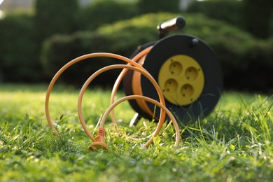 Photo of One extension cord reel on green grass outdoors, selective focus