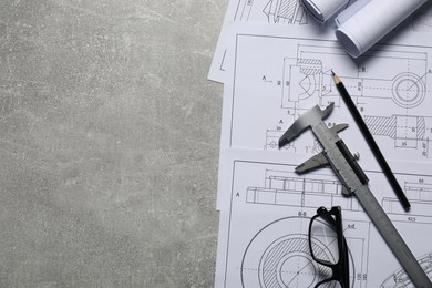 Different engineering drawings, vernier caliper, pencil and glasses on gray textured table, top view. Space for text