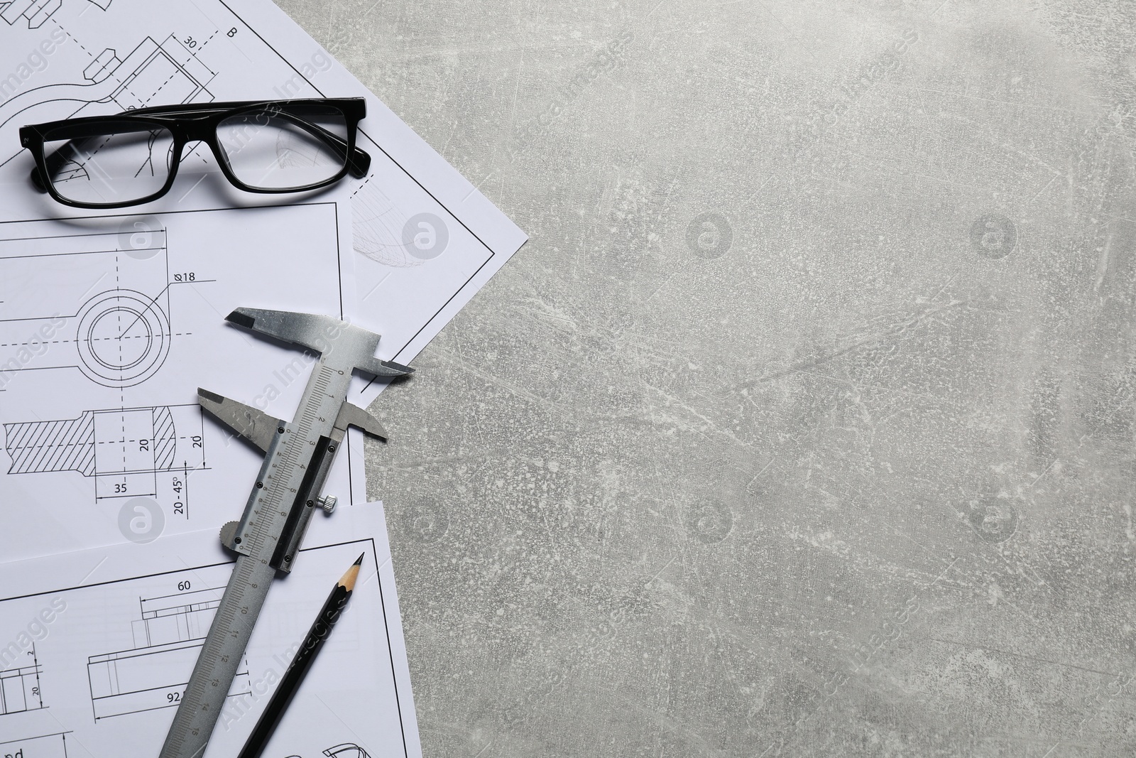 Photo of Different engineering drawings, vernier caliper, pencil and glasses on gray textured table, top view. Space for text