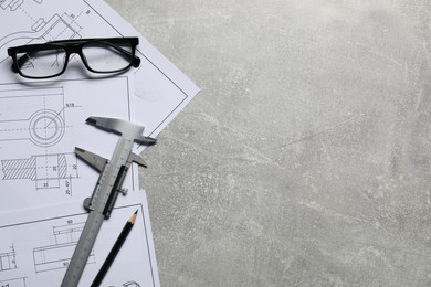 Different engineering drawings, vernier caliper, pencil and glasses on gray textured table, top view. Space for text