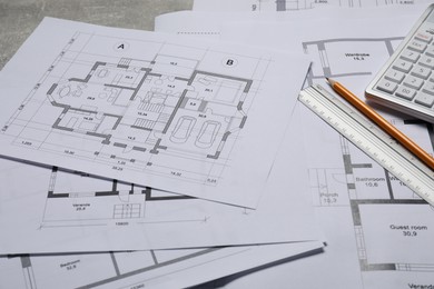 Different architectural drawings, calculator, ruler and pencil on gray table, closeup