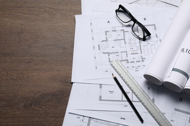 Different architectural drawings, glasses, ruler and pencil on wooden table, top view. Space for text