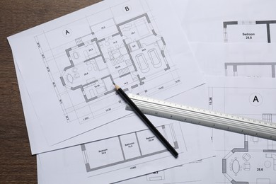 Different architectural drawings, ruler and pencil on wooden table, top view