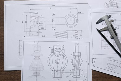 Different engineering drawings, vernier caliper and pencil on wooden table, top view