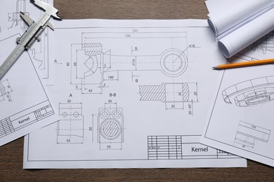 Photo of Different engineering drawings, vernier caliper and pencil on wooden table, top view