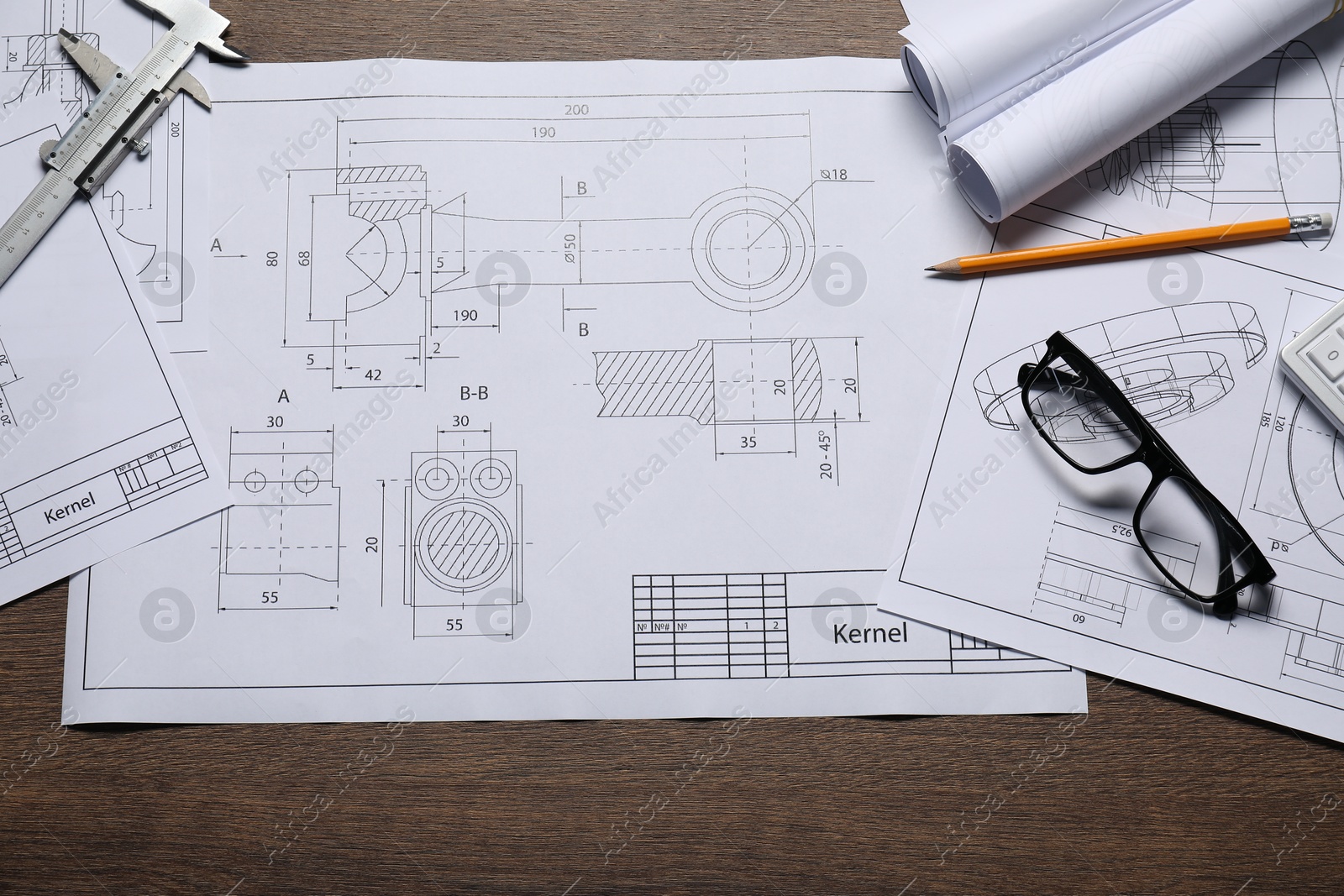 Photo of Different engineering drawings, glasses, vernier caliper and pencil on wooden table, top view