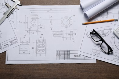 Different engineering drawings, glasses, vernier caliper and pencil on wooden table, top view