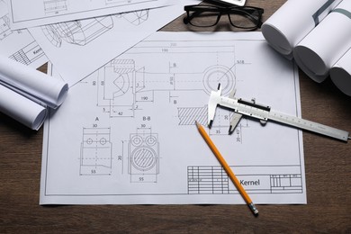 Different engineering drawings, glasses, vernier caliper and pencil on wooden table, flat lay