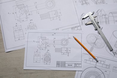 Different engineering drawings, vernier caliper and pencil on wooden table, top view