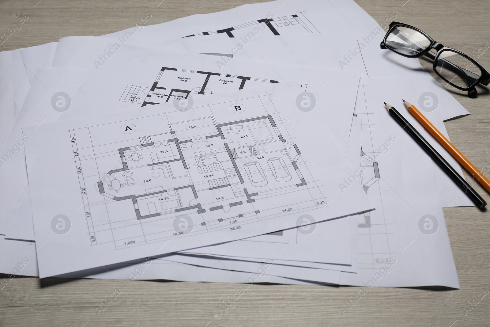 Photo of Different architectural drawings, glasses and pencils on wooden table, closeup