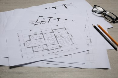 Different architectural drawings, glasses and pencils on wooden table, closeup