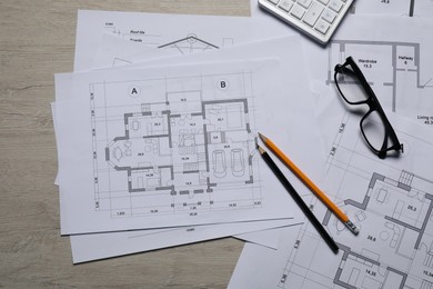 Different architectural drawings, calculator, glasses and pencils on wooden table, top view