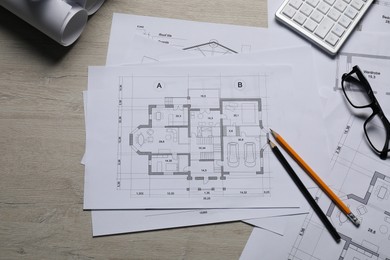 Different architectural drawings, calculator, glasses and pencils on wooden table, top view