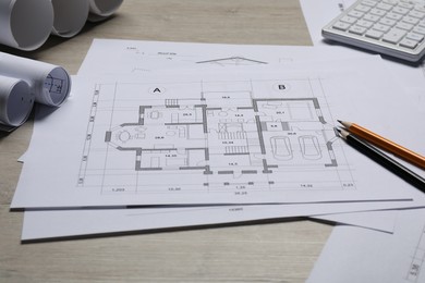 Different architectural drawings, calculator and pencils on wooden table, closeup