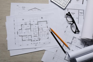 Photo of Different architectural drawings, calculator, glasses and pencils on wooden table, top view